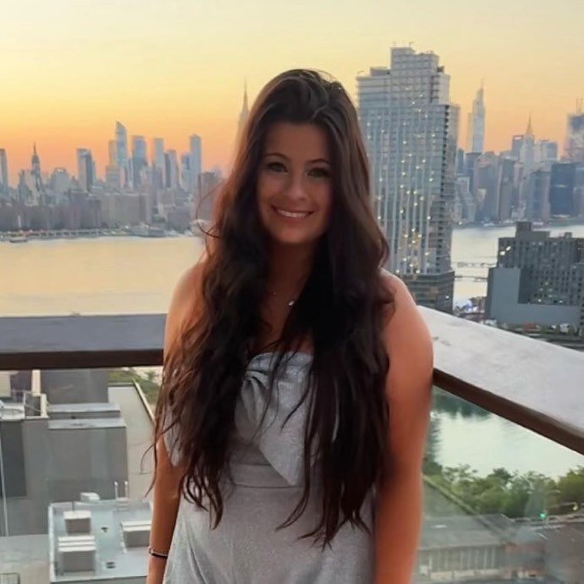 Janine smiling on a rooftop at sunset with the city skyline behind her